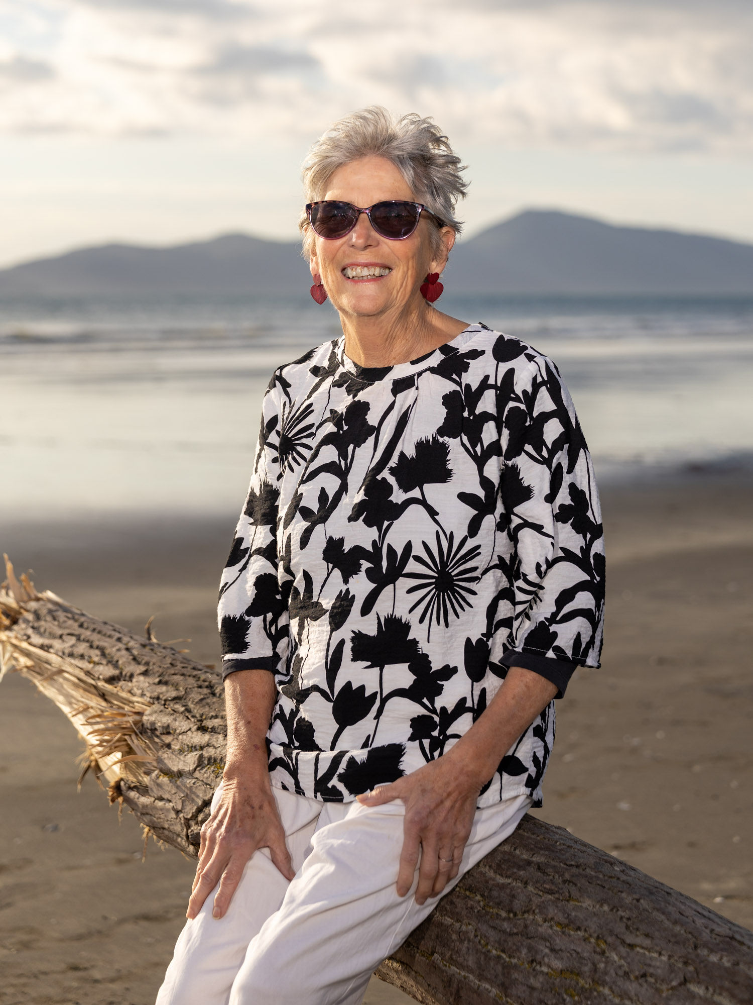 Jude Castle smiling on a beach on the Kāpiti Coast, with the sea and hills behind her